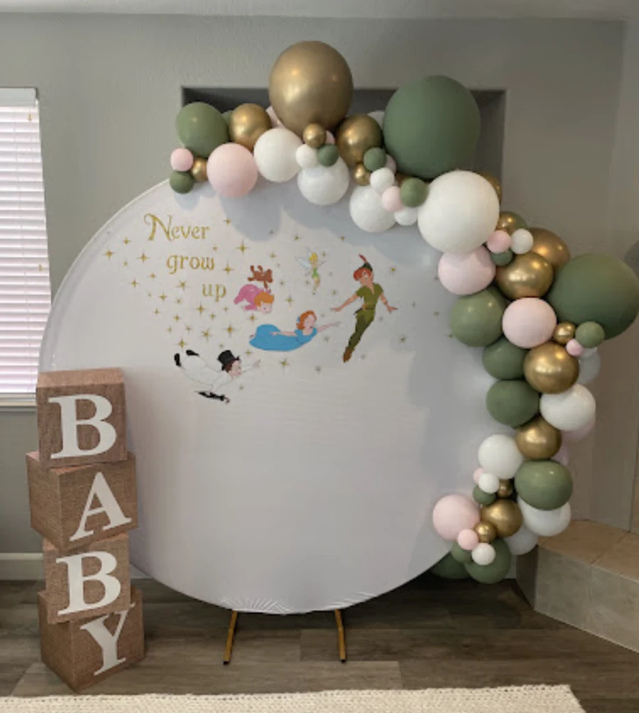 Soft green, cream, blush and gold balloon garland around a Never grow up baby shower backdrop.