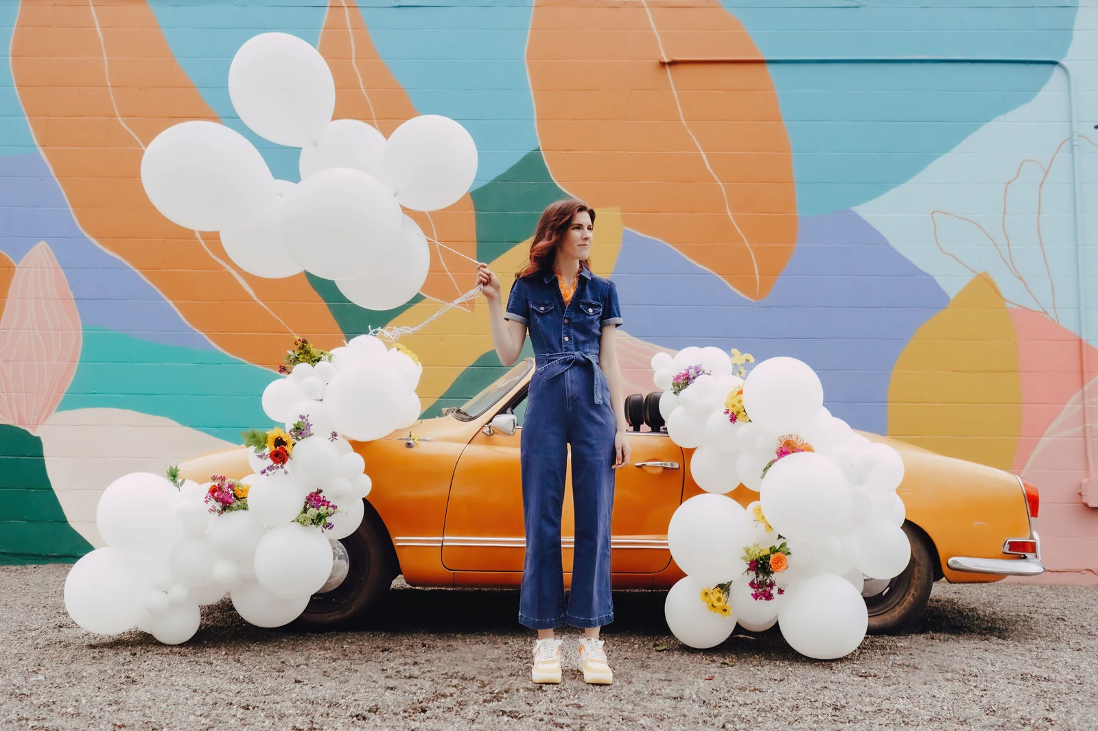 Karlie holding white balloons beside an orange convertible decorated with balloons and flowers.