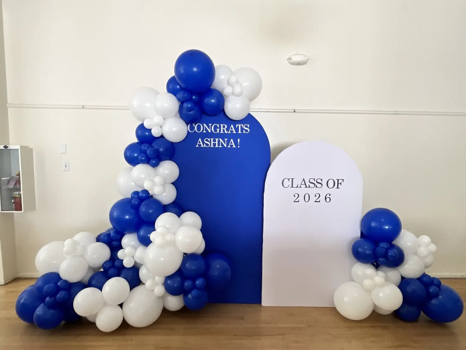 Royal blue and white balloon garland around a graduation backdrop with an arched Class of 2026 panel