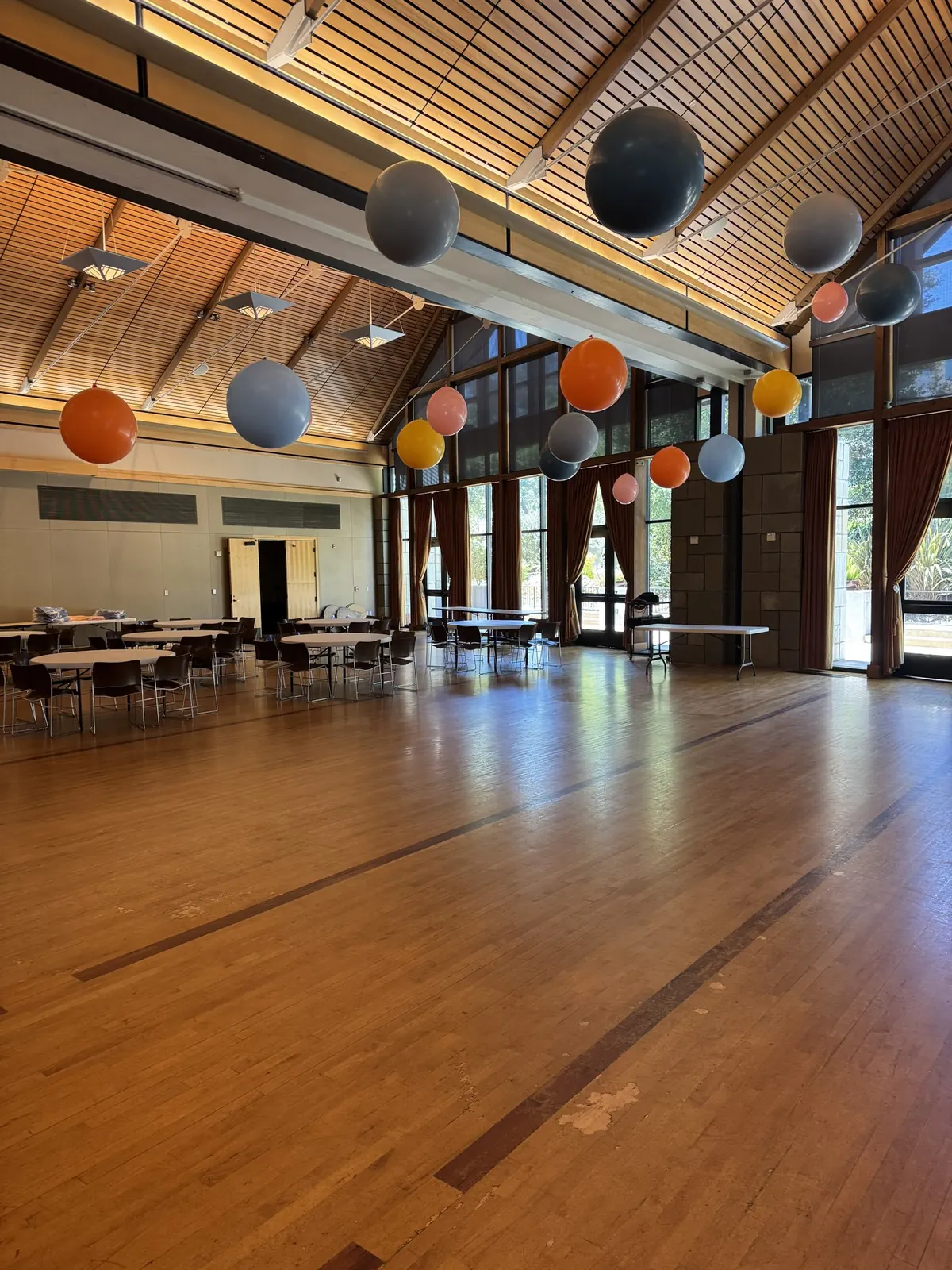 Oversized gray, blue, and orange balloons suspended from the wood beamed ceiling of a large event hall