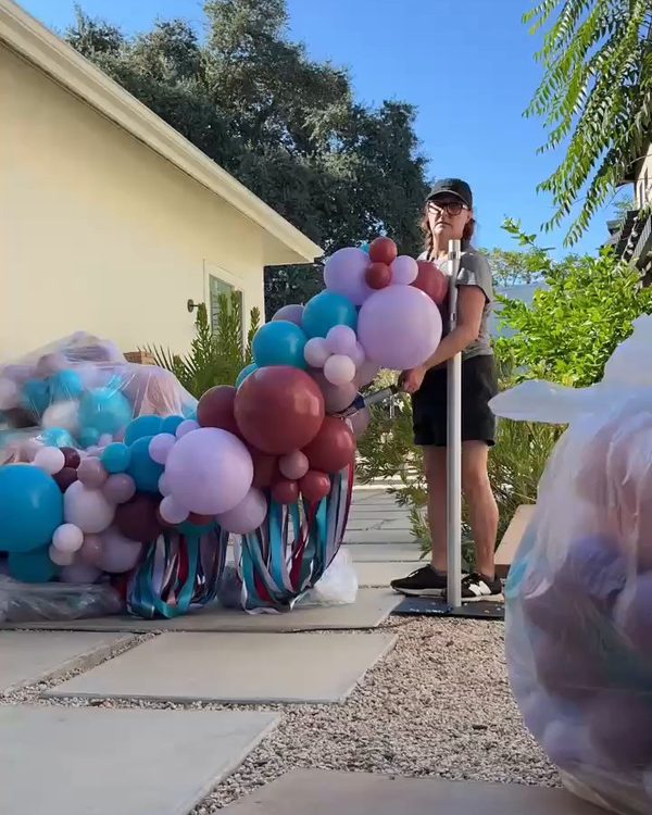 Poptastic Parties team member setting up a pole of the squared balloon arch frame on a garden path in Danville next to teal and burgundy balloon garlands