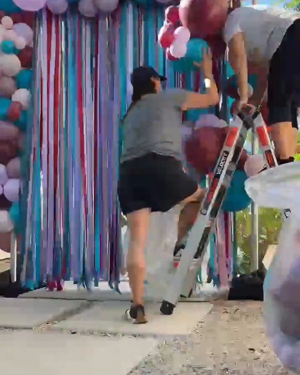 Two team members adding mauve and burgundy balloons to the side of the squared balloon arch in Danville in front of the ribbon curtain