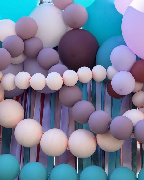 Close up of teal, mauve, blush, lavender and burgundy balloon strands looping over the ribbon curtain of the Danville squared balloon arch