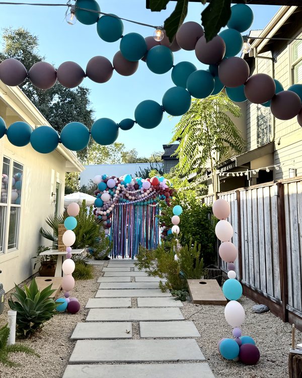 Garden path in Danville lined with blush and teal helium balloon columns under teal and mauve link balloon strands, leading to the squared balloon arch and ribbon curtain