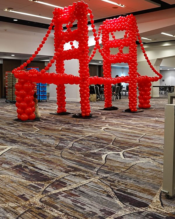 Finished red Golden Gate Bridge balloon sculpture with two towers, roadway and suspension cables in a San Francisco Marriott Marquis ballroom
