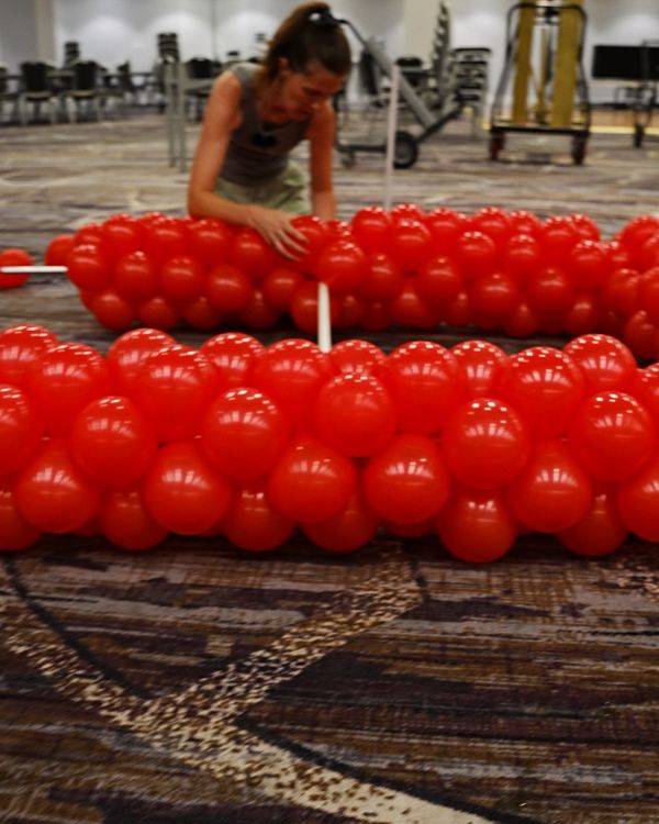 Red balloon tower sections laid out on the carpet of the Golden Gate Room in San Francisco before being joined to the frame