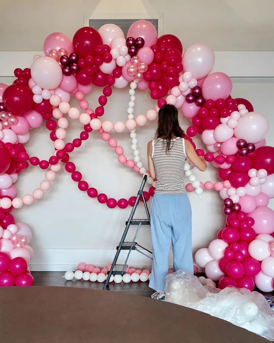 Holding a white link balloon strand in front of fuchsia and pink link balloons already draped across the arch
