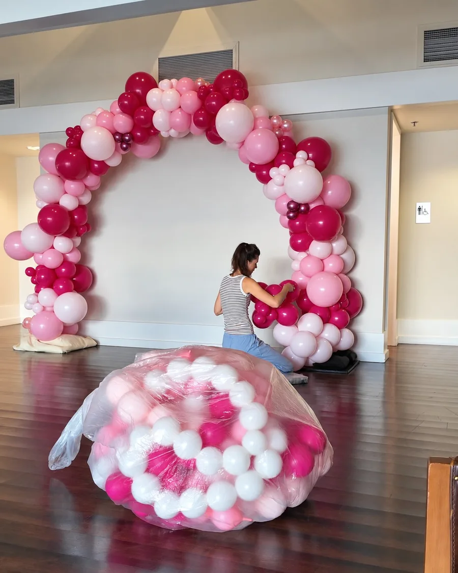 Kneeling to add more balloon clusters to the bottom of a standing pink balloon arch
