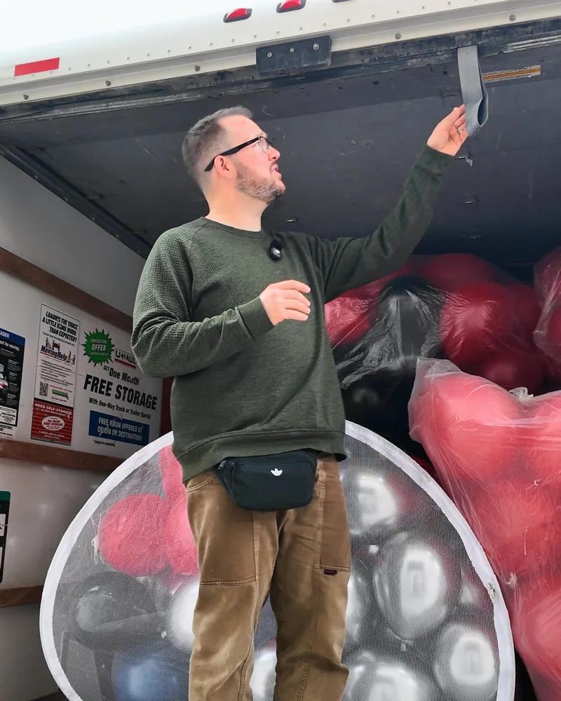 Kyle standing in the back of a rental truck beside a filled balloon drop net before driving to a school in San Jose