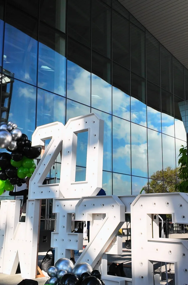 Early balloon clusters on the side of white 2026 HW FEST marquee letters outside a glass building in Santa Clara