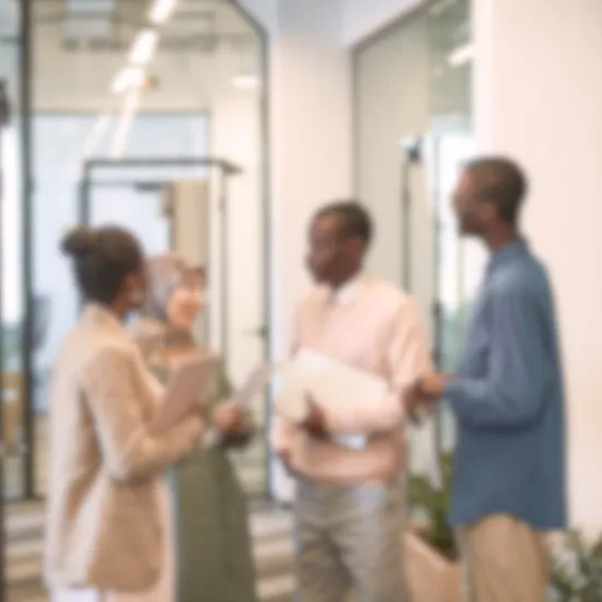 A blurred image captures four people in an office setting, engaged in a professional discussion likely focused on business growth. They hold folders and documents, with glass walls and office furniture visible in the background.