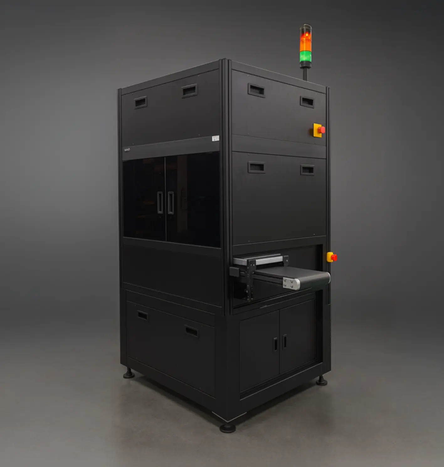 Large black industrial machine with a small conveyor belt, emergency stop buttons, and red and green indicator lights on top.