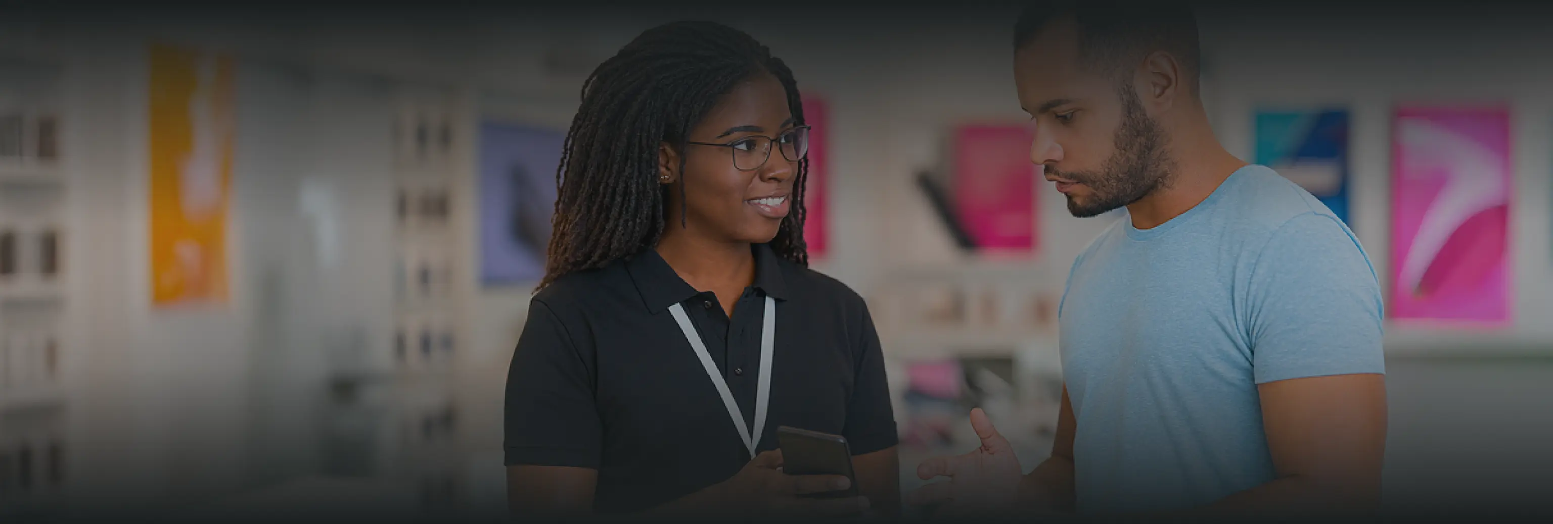 Saleswoman smiling and showing a smartphone to a male customer in a retail store.