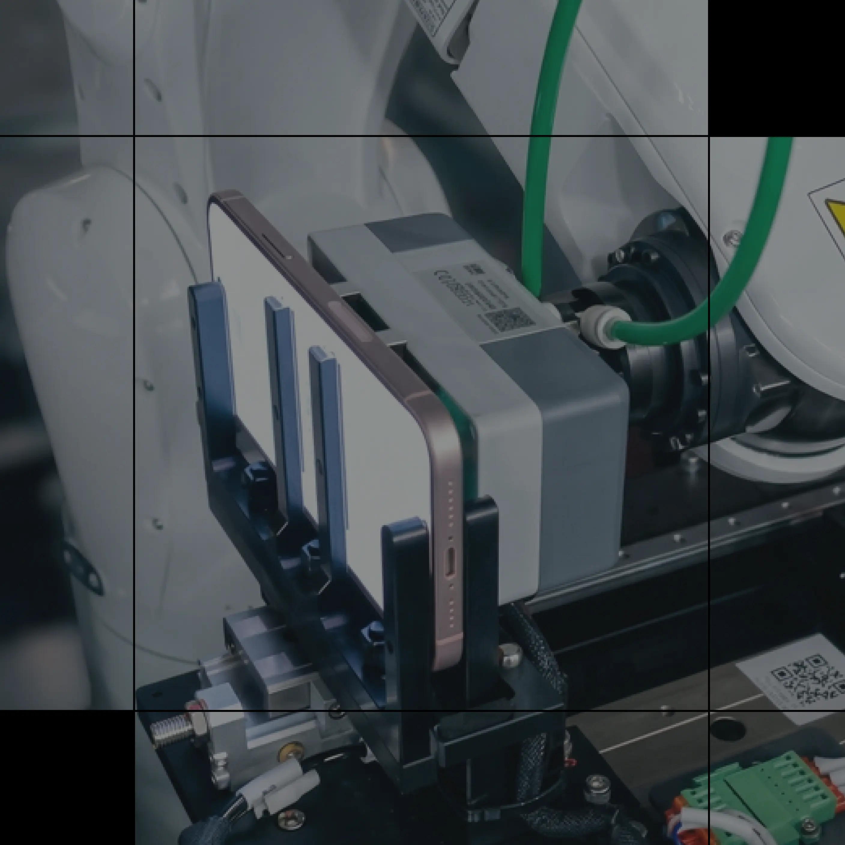 Robotic arm holding several smartphones mounted in a testing rig with connected cables.