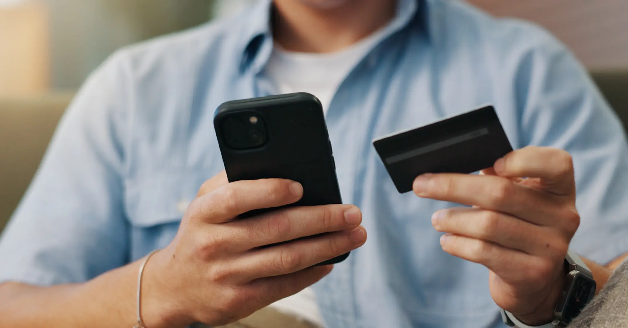 Person holding a black smartphone in one hand and a black credit card in the other.