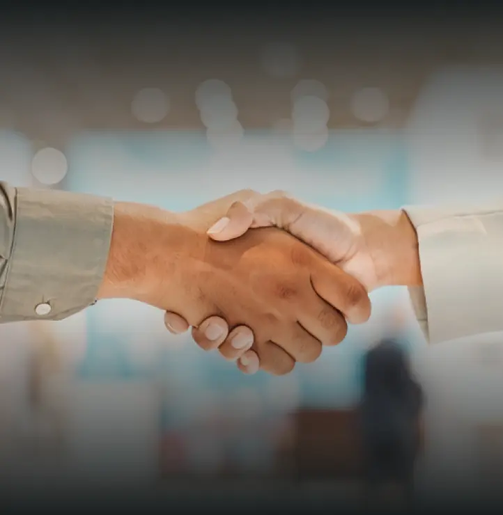 Close-up of two people shaking hands in a blurred office setting.