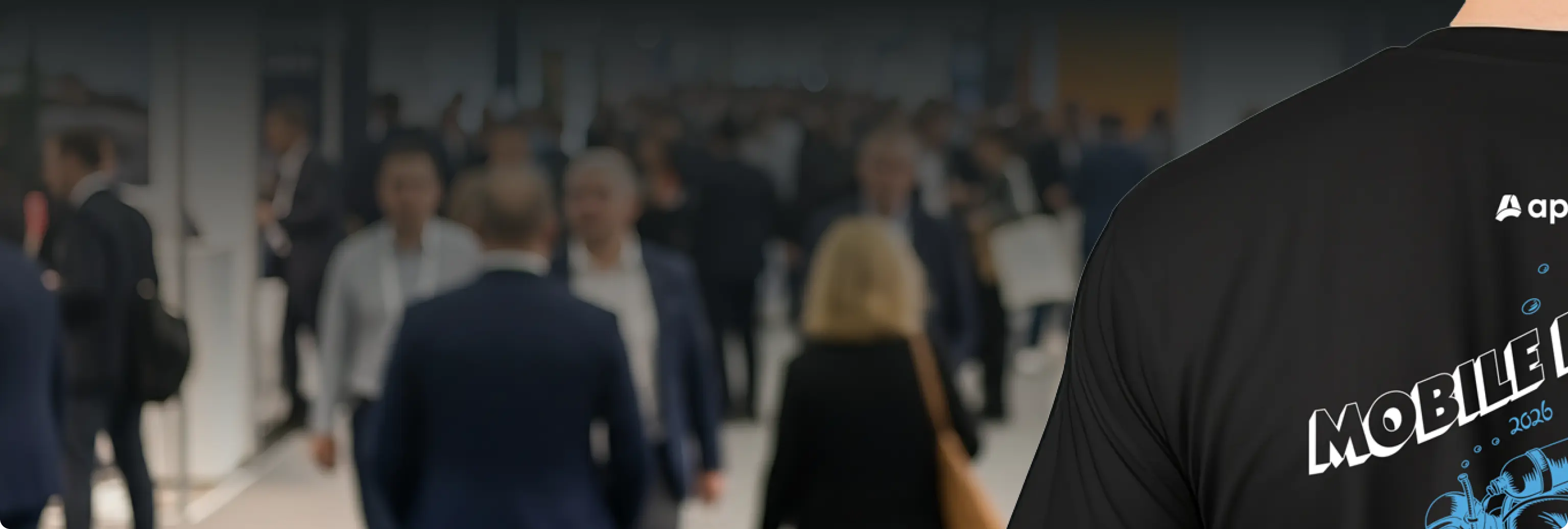 Crowd of people in business attire at an indoor event with a person wearing a black Mobile Disrupt shirt.