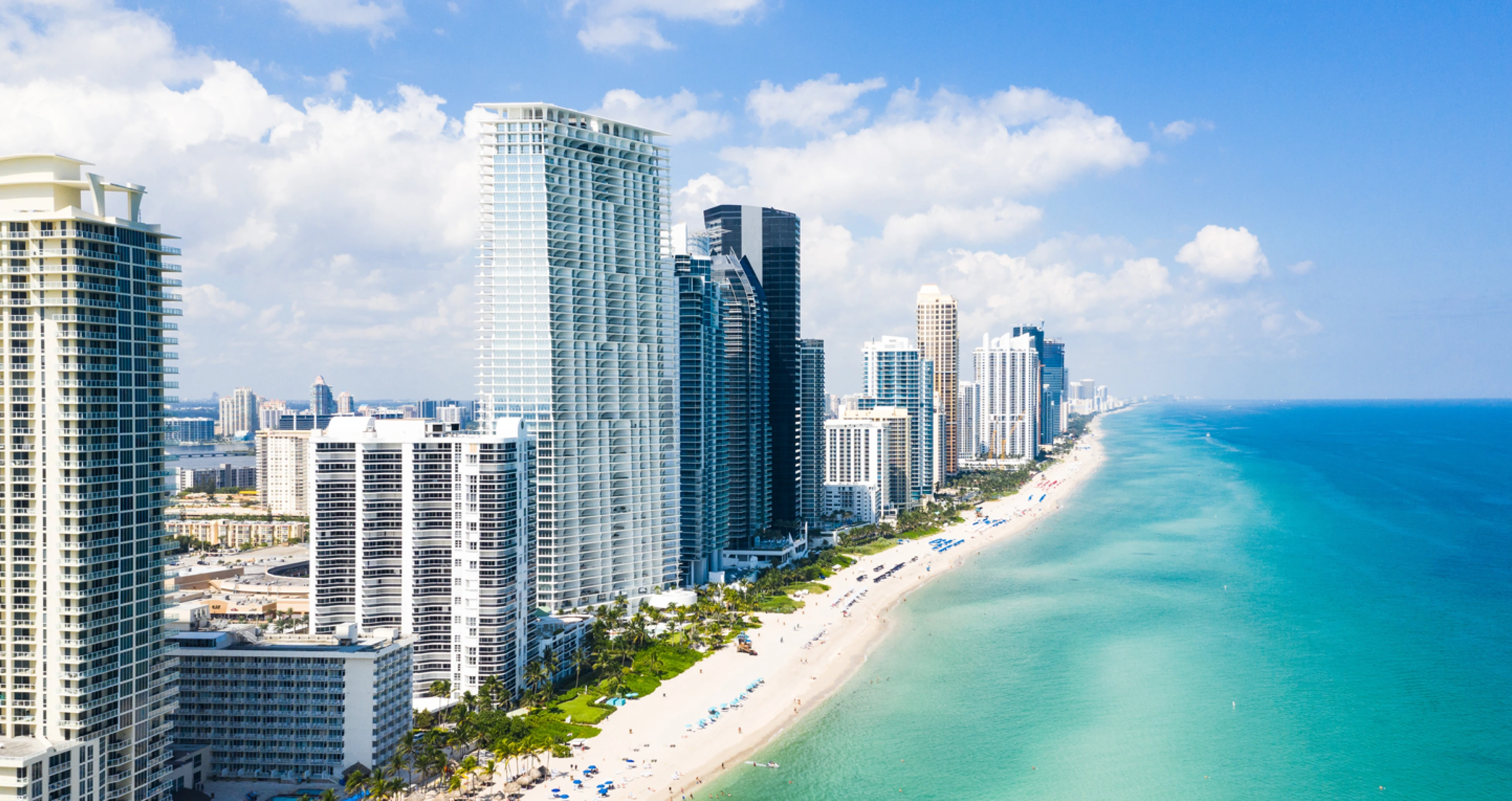 Aerial view of a beach with tall buildings along the shoreline and turquoise ocean water.