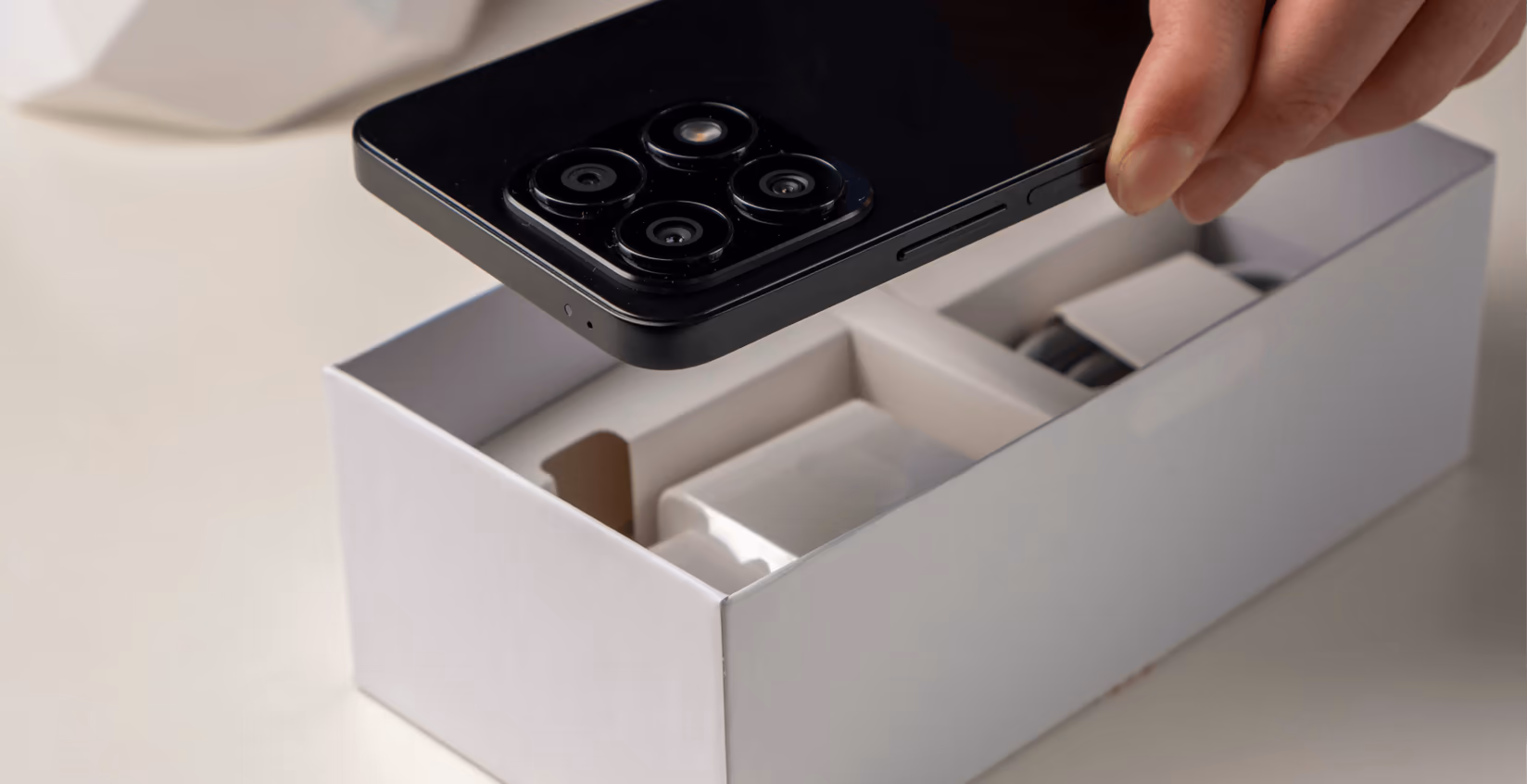 Hand lifting a smartphone out of a white packaging box