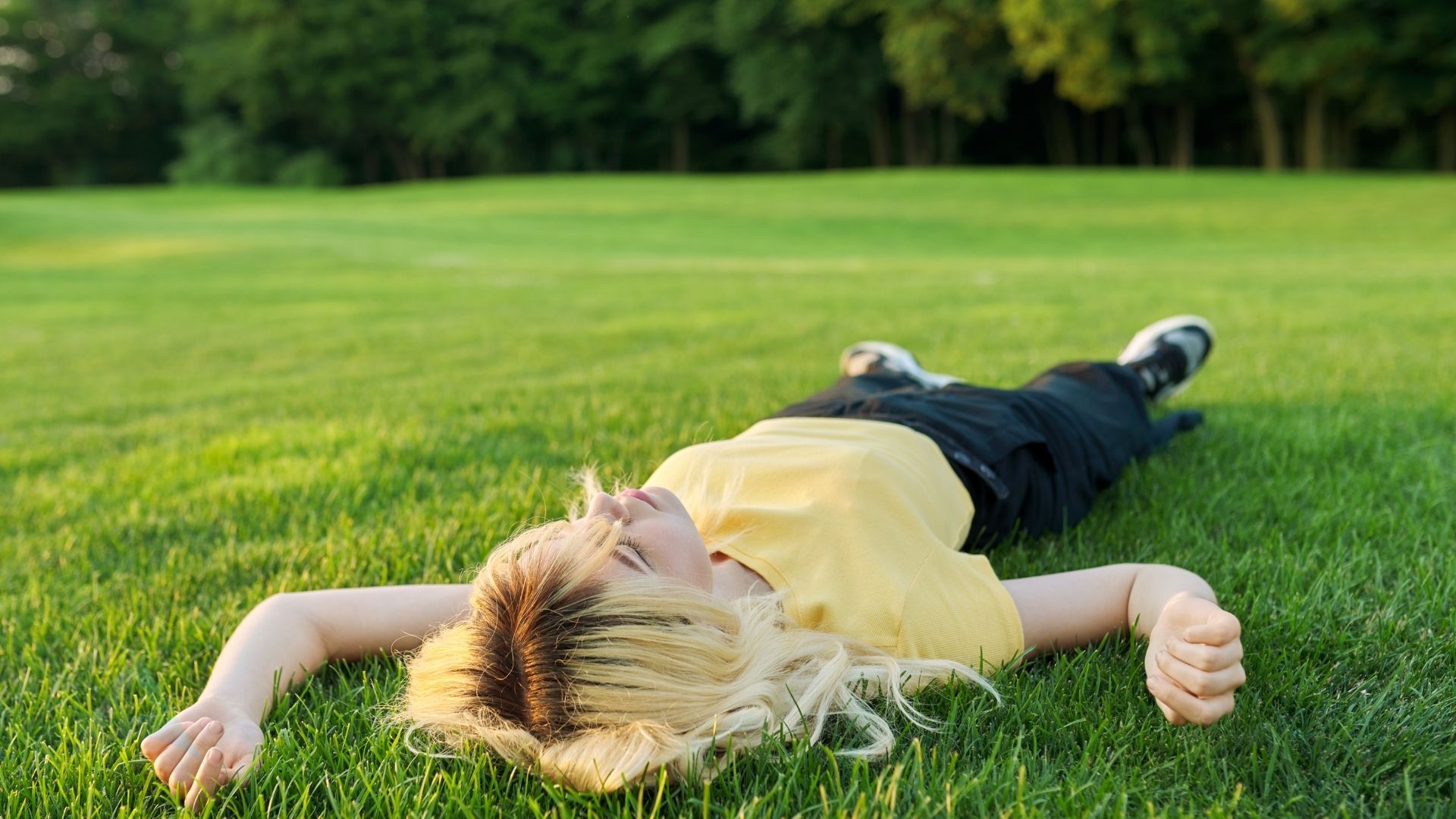 Person sitting in a garden with hands pressed on grass representing the intentional grounding practice that supports nervous system healing and stress reduction