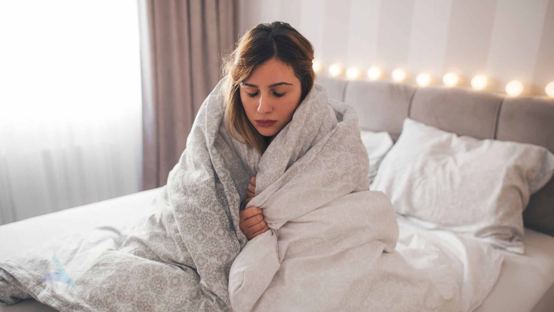 Person wrapped in a blanket holding a warm mug by a window, representing living with fibromyalgia and chronic pain in Boise