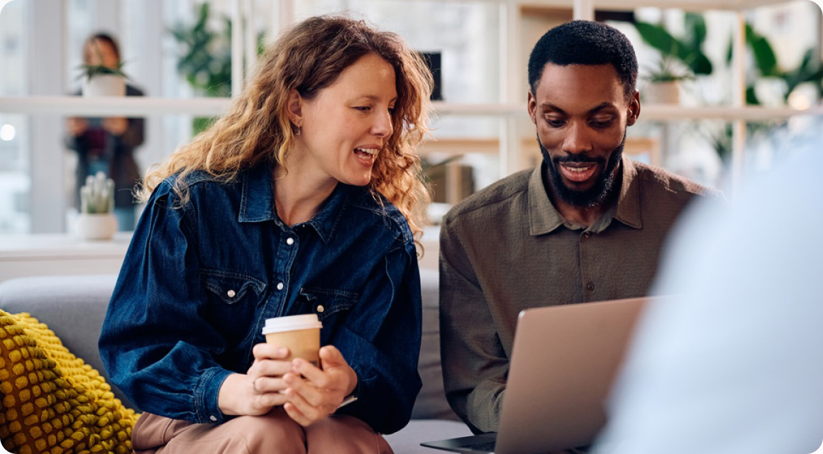 Two coworkers smiling while reviewing benefits on a laptop