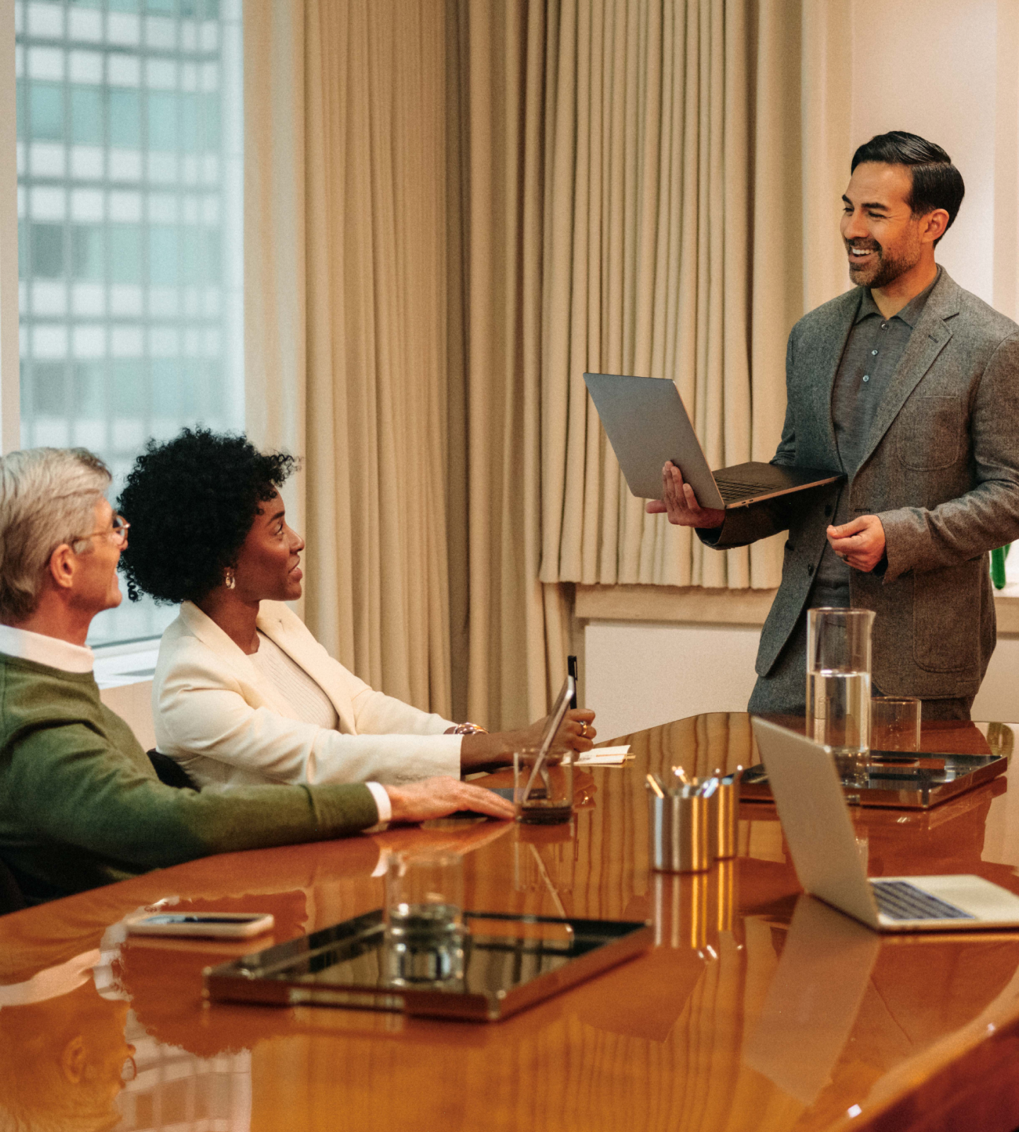 Image of a man holding a laptop smiling during a meeting