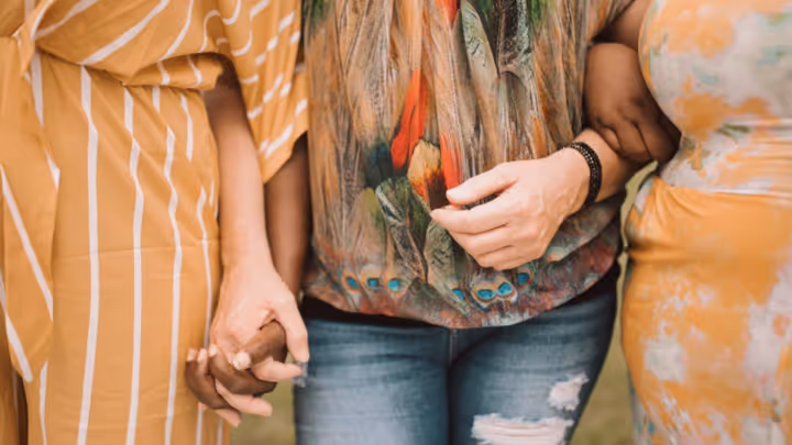 Three people standing side by side holding hands, wearing colorful patterned clothing.