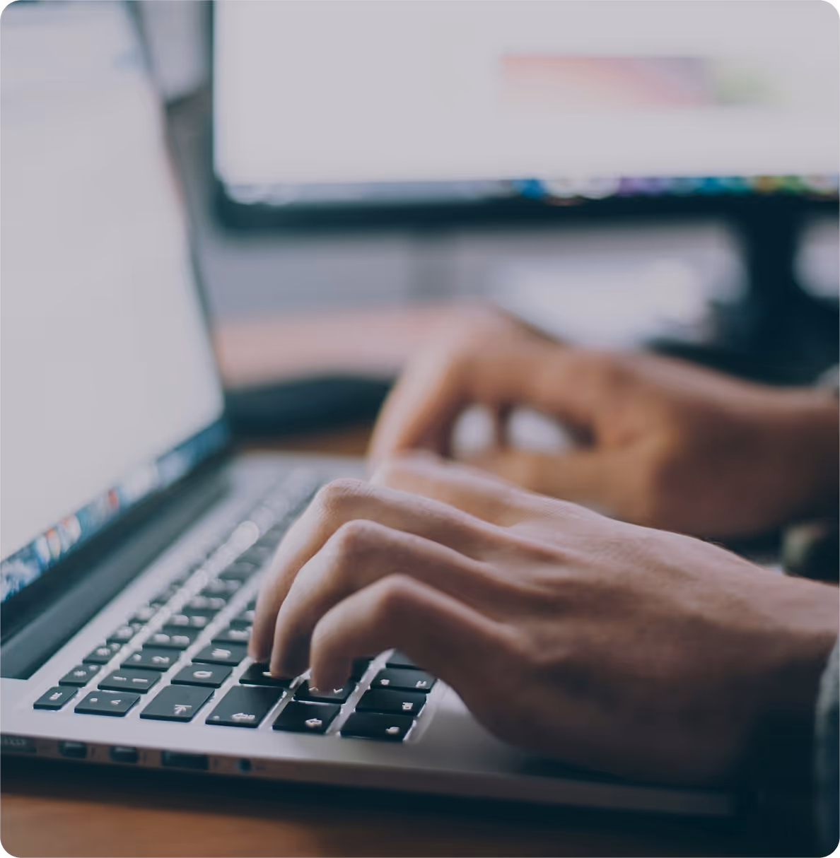 Person working on an apple laptop at a desk with a second monitor