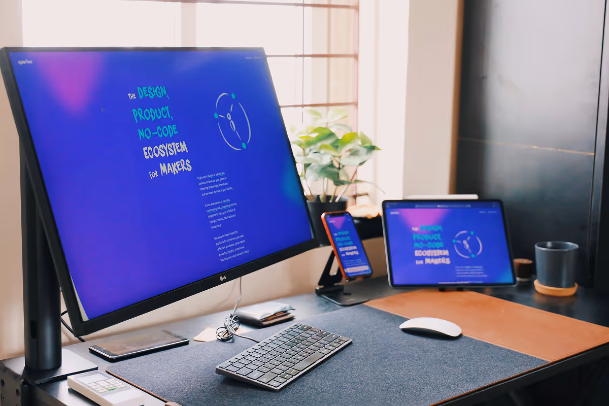 Modern workspace with a large monitor, tablet, and smartphone displaying a colorful design and no-code ecosystem text.