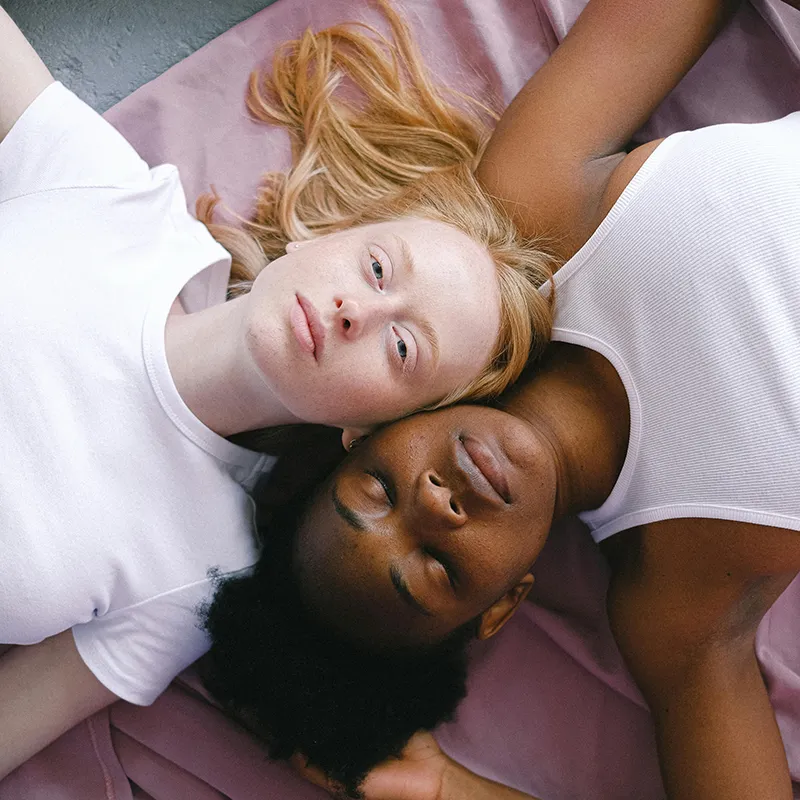 Two mixed race women sitting on a pink blanket