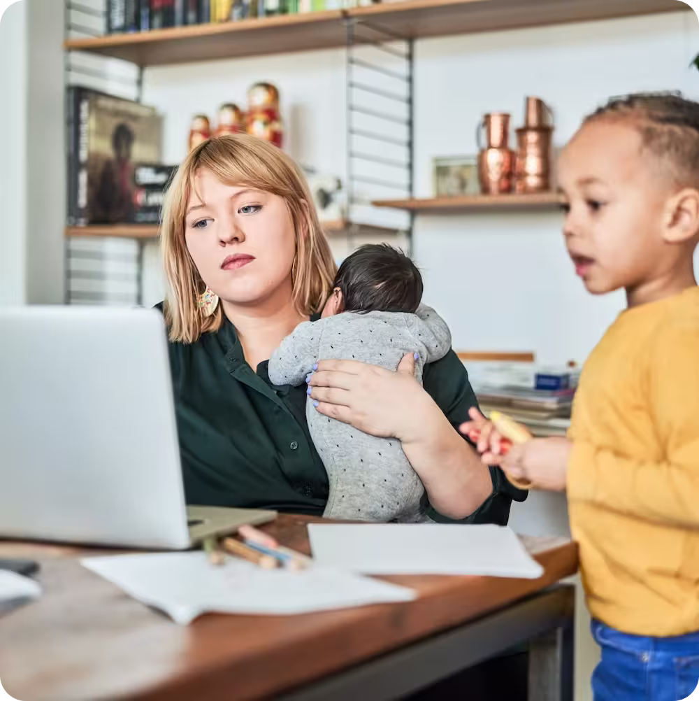 A woman holding a child in front of a laptop computer.
