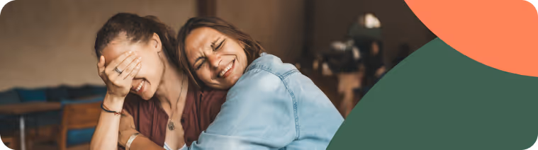 Mother and daughter laughing and hugging in a coffee shop.