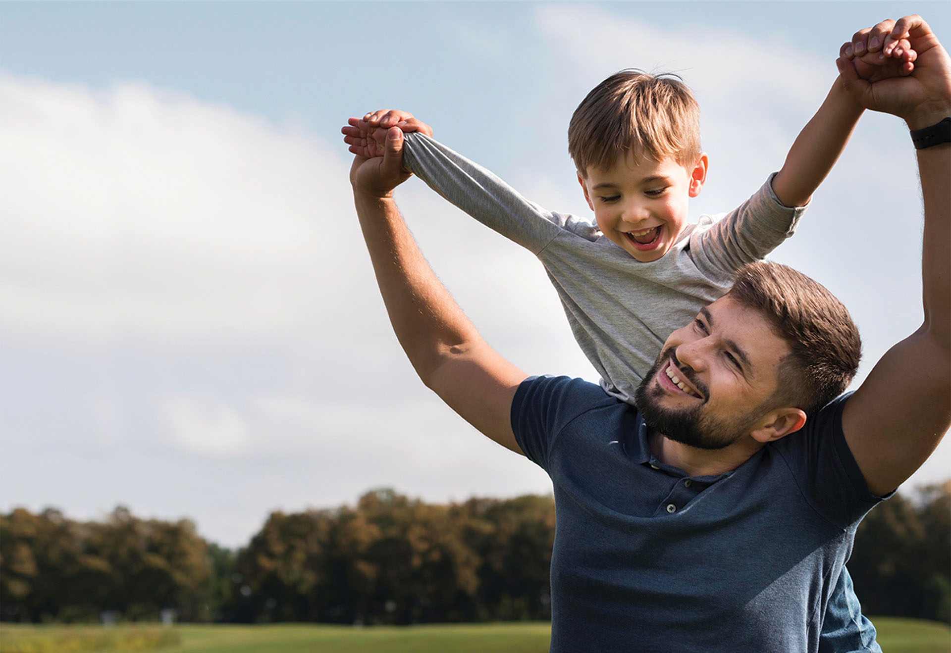 Hero background image of a smiling father giving his son a piggyback.