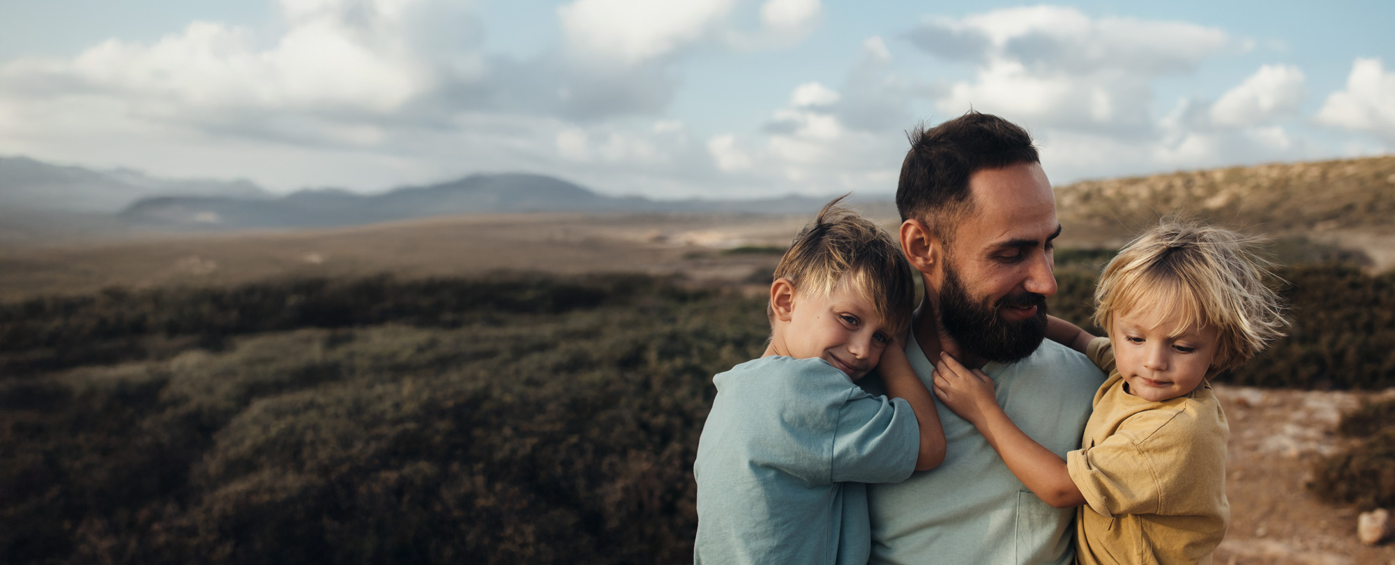 Hero background image of a smiling father holding his two children