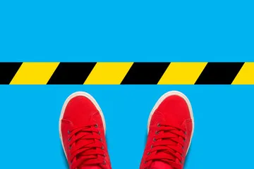 Female feet in red sneakers standing in front of a warning black-and-yellow line. Concept of the destruction of borders and violations of the rules. Flat lay, top view