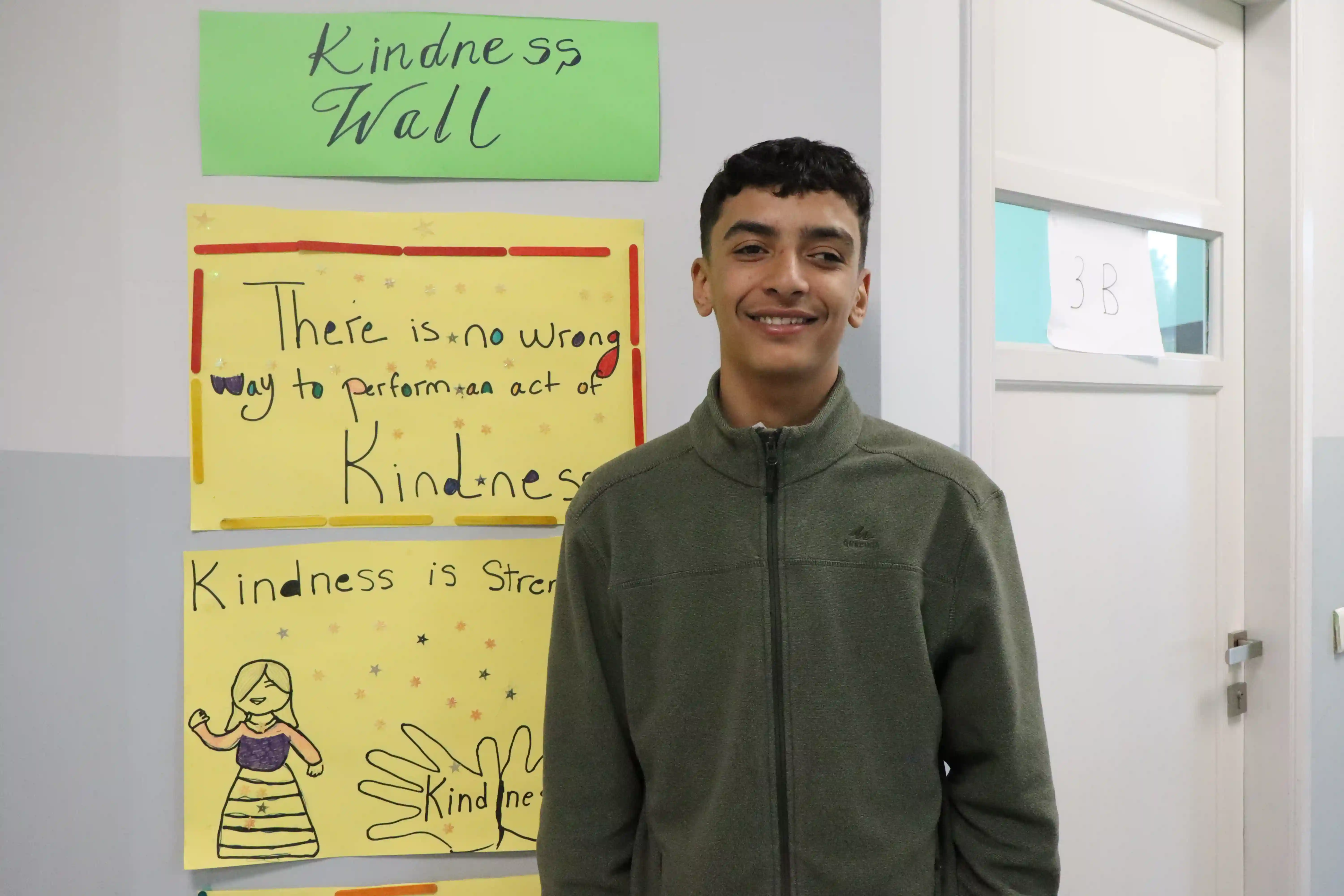 Samir smiling as he stands in front of the "Kindness Wall" in his classroom.