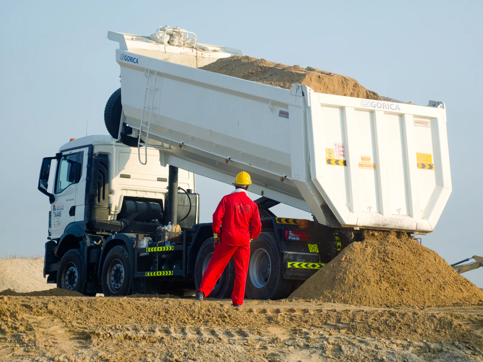 Camion benne déchargeant des matériaux devant un opérateur