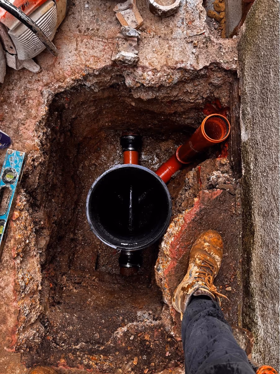 A person stands by a freshly installed drainage pipe in a dug-out section of ground.