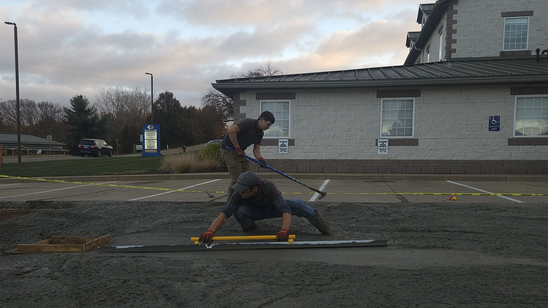 Two concrete workers leveling concrete in a parking lot