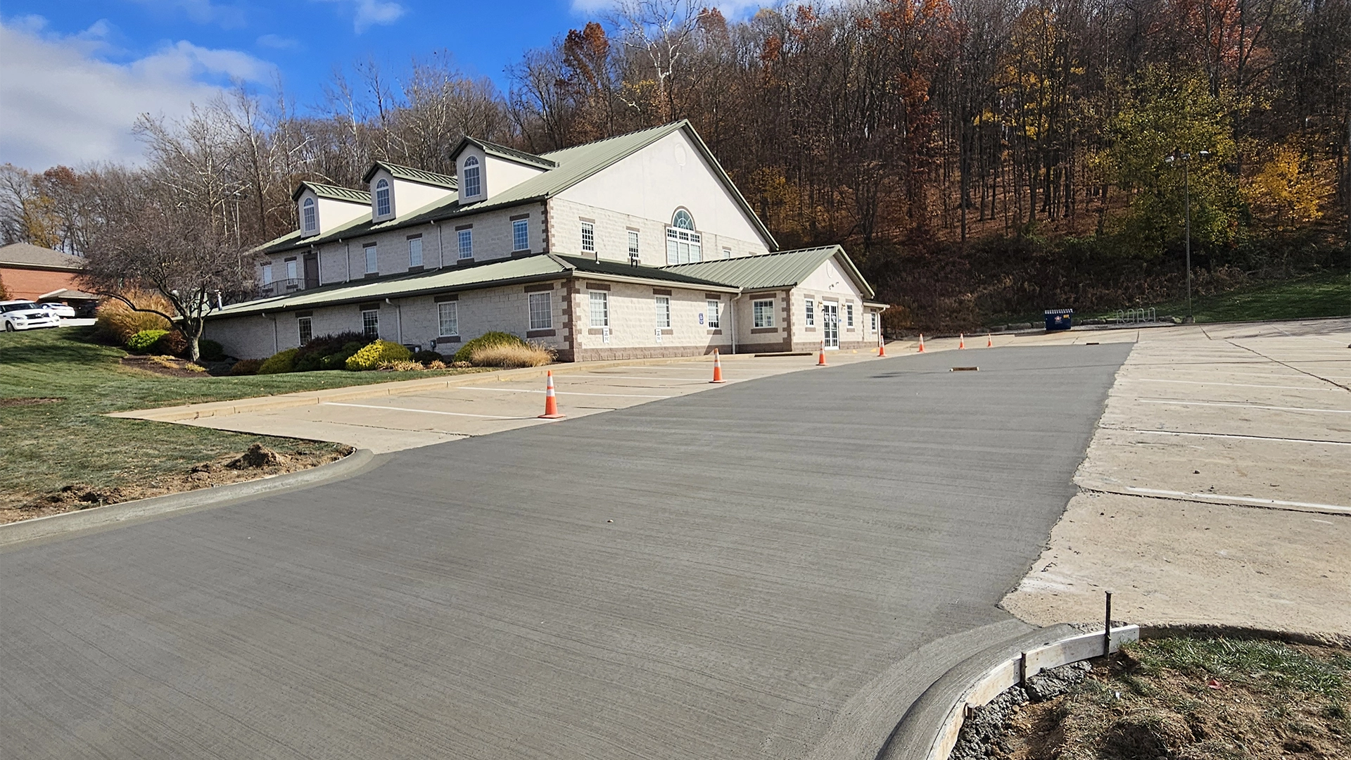 a newly finished concrete driveway going uphill leading to a two story building with a green metal roof tan stones and cream colored siding
