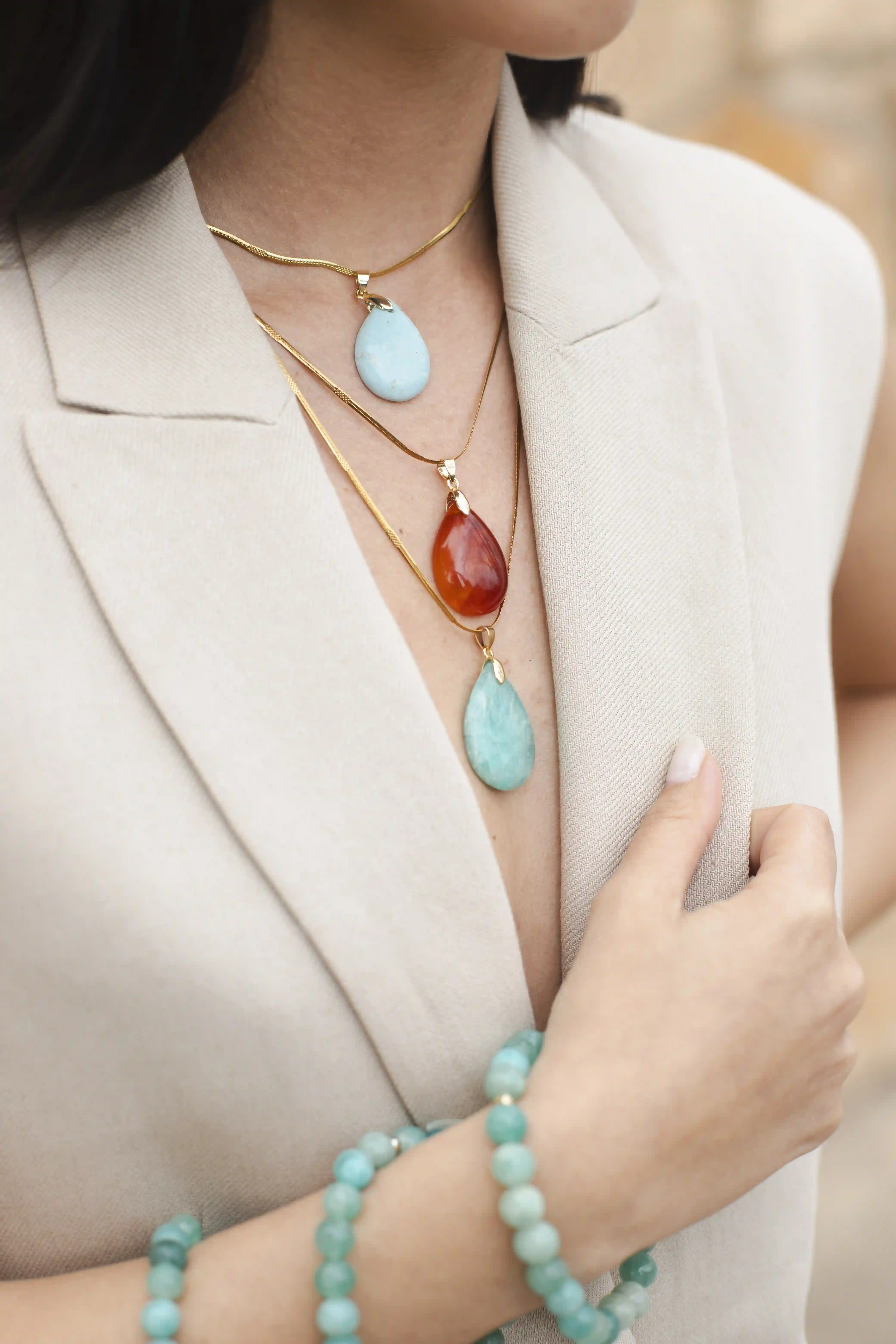 Close-up du décolleté d’une femme en blazer, portant trois médaillons dont deux bleus en opaline et un rouge en cornaline, mis en valeur sur la peau.