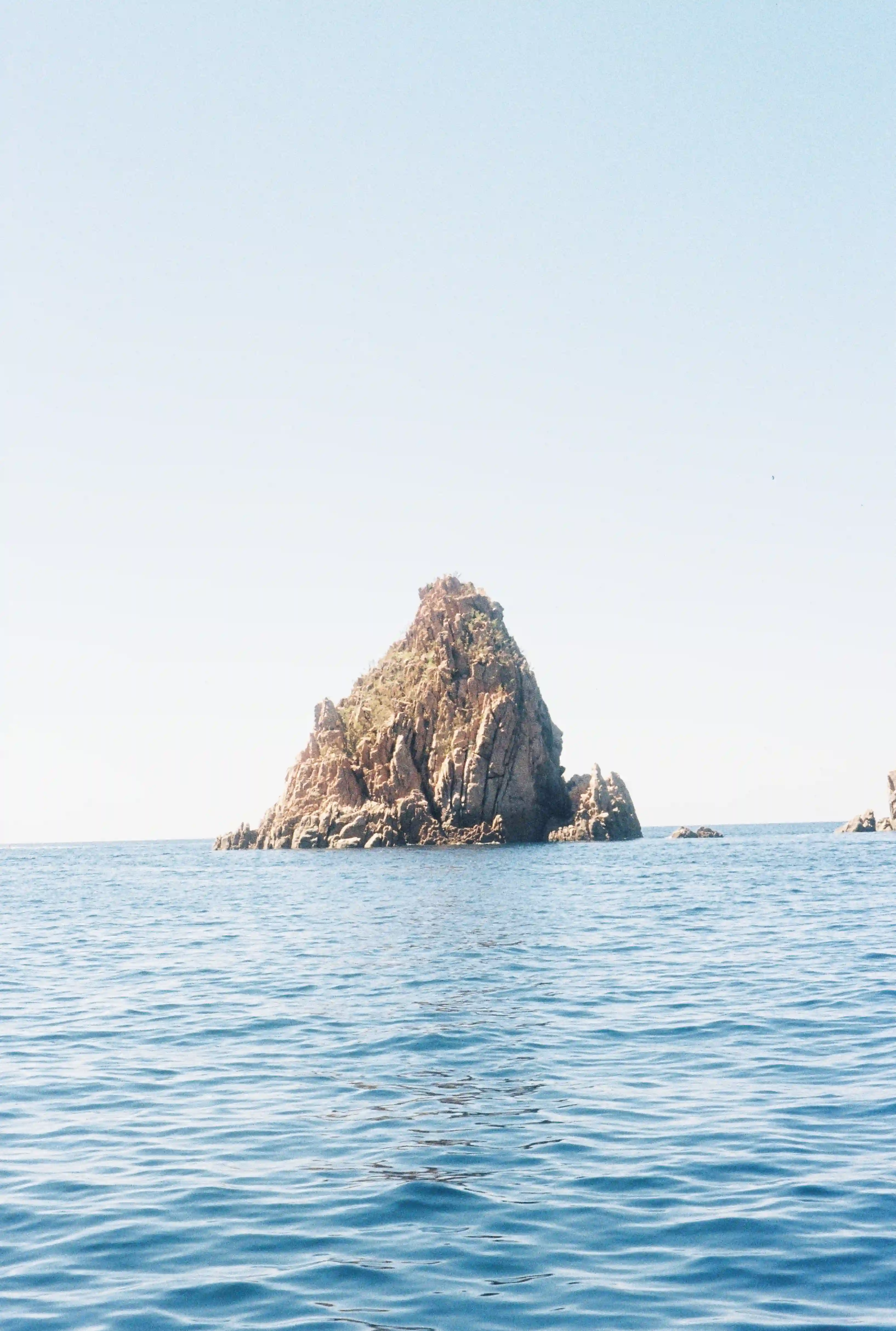 Petite île entourée par la mer en plein soleil, paysage lumineux et dégagé.