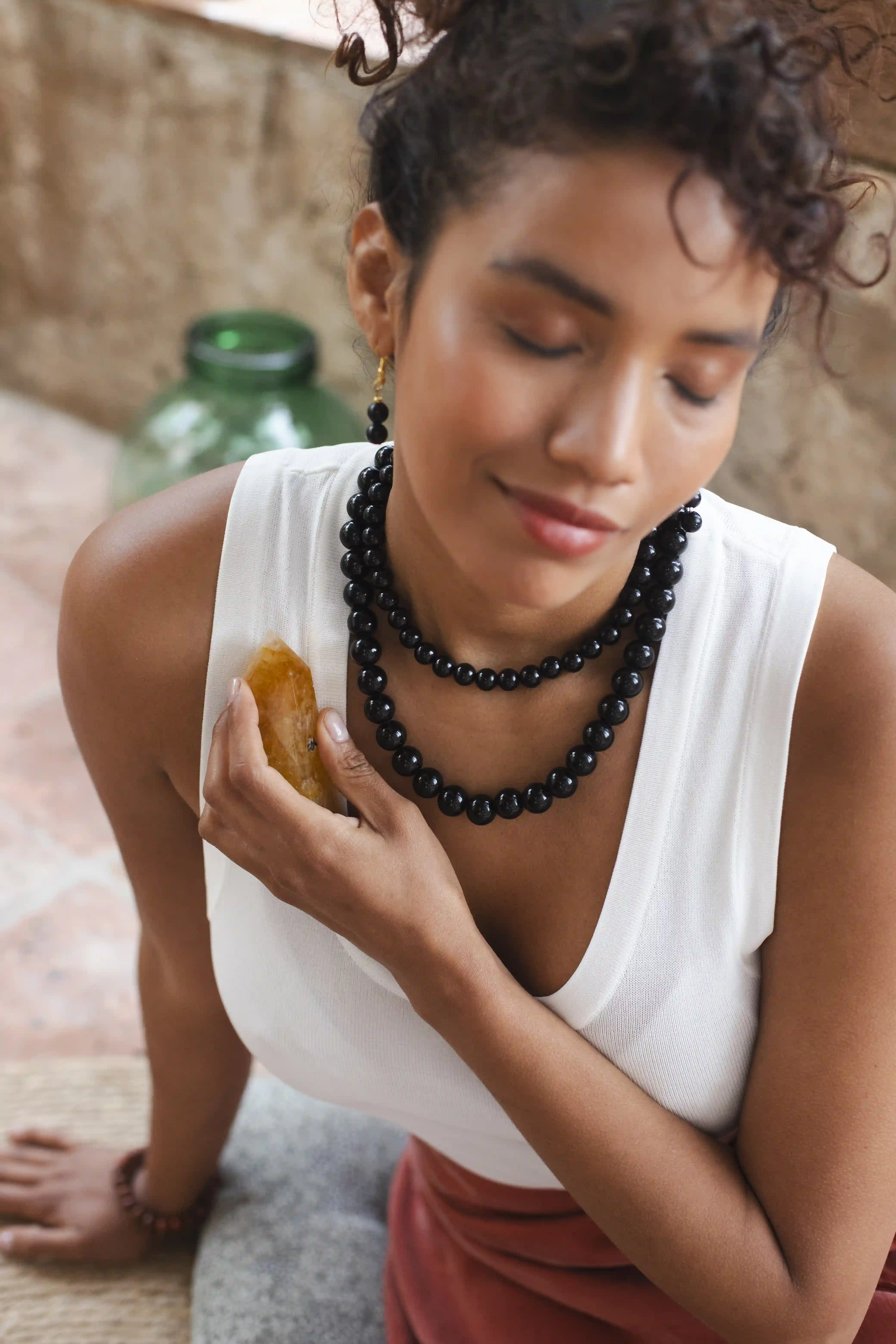 Celeste Beas, modèle à Barcelone dans une ambiance chic et estivale, portant un débardeur blanc, deux gros colliers noirs et une pierre naturelle près du cœur.