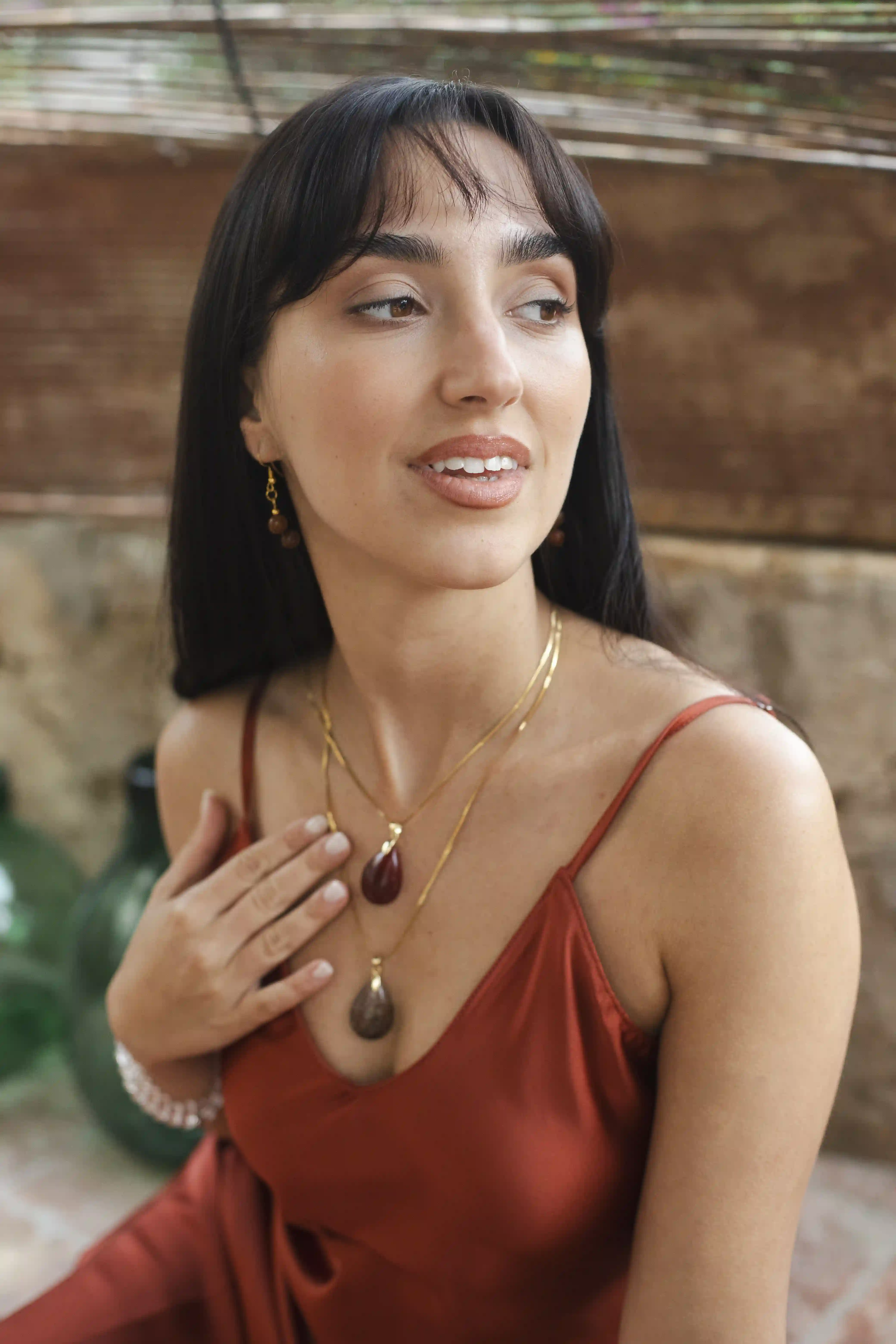 Modèle assise à Barcelone dans une ambiance chic et estivale, regardant au loin tout en touchant ses colliers à pendentifs en pierre naturelle.