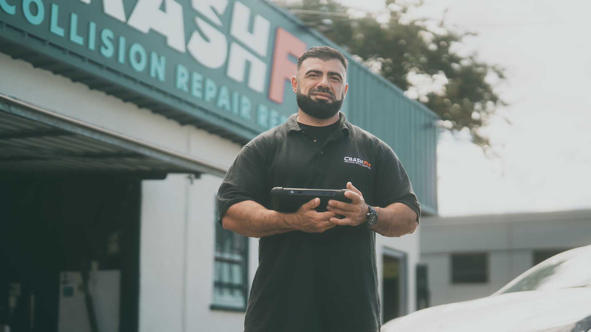 CrashFix Technician standing in front of CrashFix Auto Body Shop with Diagnostic tools