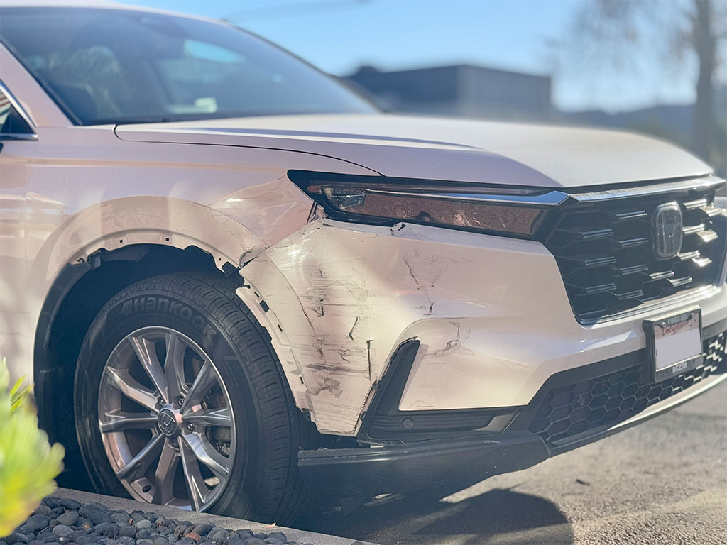 Honda CR-V with significant passenger-side front-end damage, including a torn bumper cover, dented fender, and scuffed headlight area