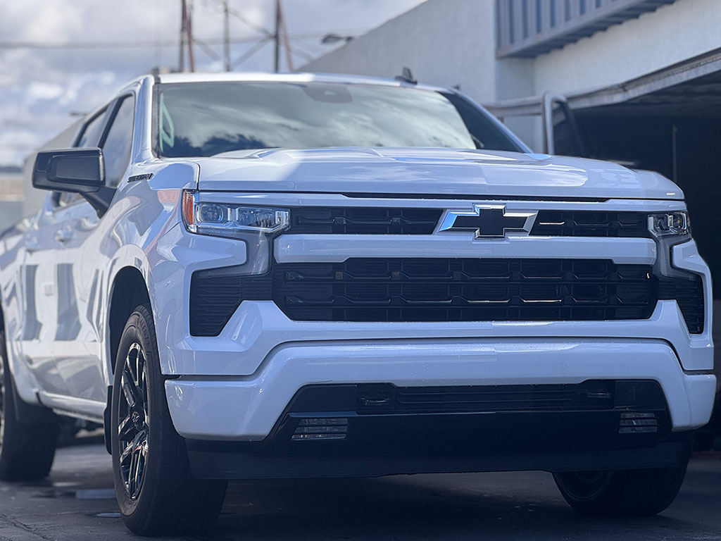Close-up front view of a repaired and restored white Chevrolet Silverado with customized all-black front fascia, perfectly finished and parked on a clean street