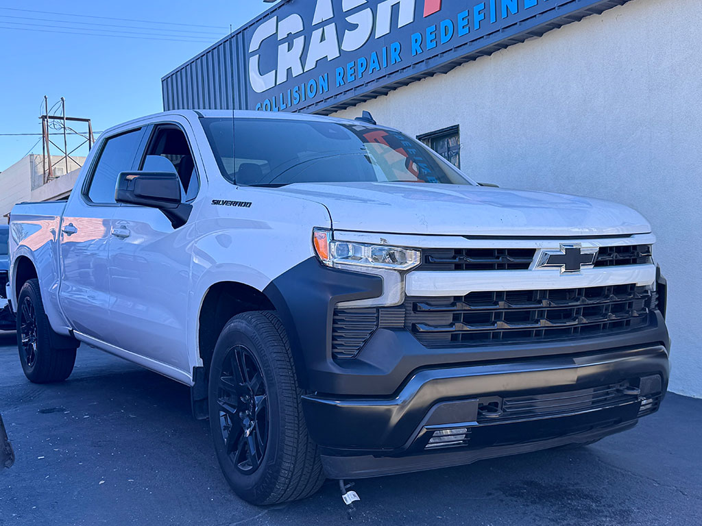 restored white Chevrolet Silverado custom crew cab truck after front-end repair with a black grille and bumper at CrashFix's interior repair bay