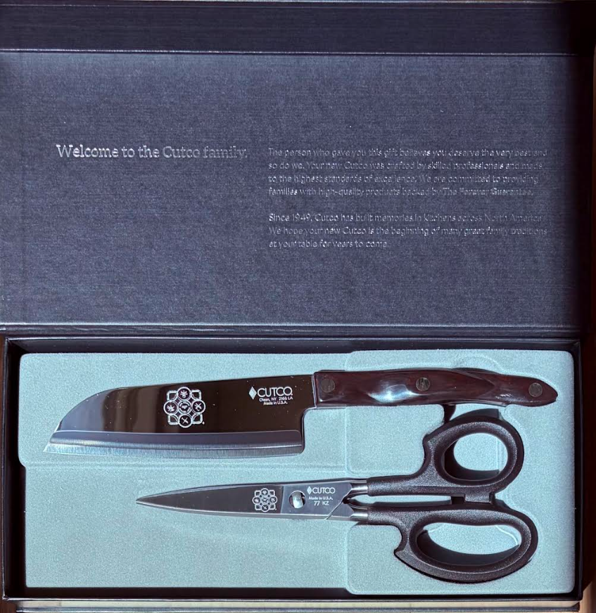 Open Cutco knife gift box showing a small serrated kitchen knife with marbled handle and a pair of black-handled scissors set in light foam padding, with a printed welcome note inside the lid.